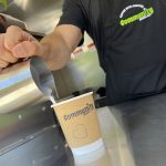 Close up of a man's hand pouring milk into a branded coffee cup